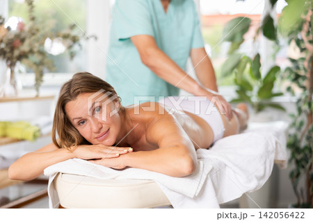 Glad middle-aged woman having hip massage done by mature masseuse Glad middle-aged woman having hip massage done by mature masseuse 142056422