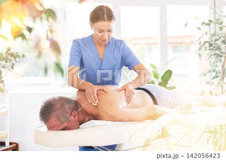 masseuse giving massage to male patient masseuse giving massage to male patient 142056423