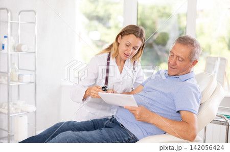 Old male patient signing papers while talking with woman doctor Old male patient signing papers while talking with woman doctor 142056424