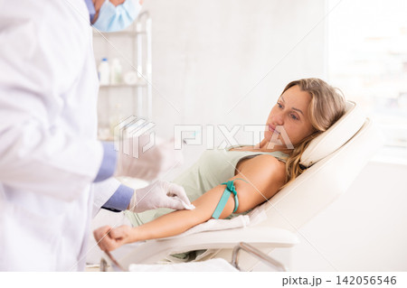 Unrecognizable male senior nurse performs procedure of blood drawing for analysis to woman 142056546