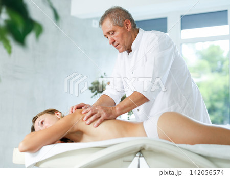 Skilled old masseur conducting back massage for woman client Skilled old masseur conducting back massage for woman client 142056574