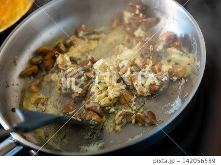 There is frying pan with scrambled eggs on stove, complemented with champignon and asparagus 142056589