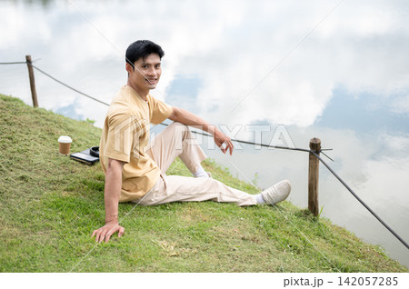 Asian Man Smiling While Relaxing Outdoors Beside a Lake Asian Man Smiling While Relaxing Outdoors Beside a Lake 142057285