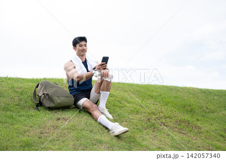 Athletic Asian Man Resting and Using Smartphone After Running 142057340