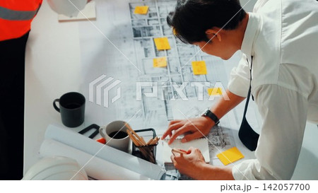 Top view of team inspect house model while manager hold blueprint. Alimentation. Top view of team inspect house model while manager hold blueprint. Alimentation. 142057700