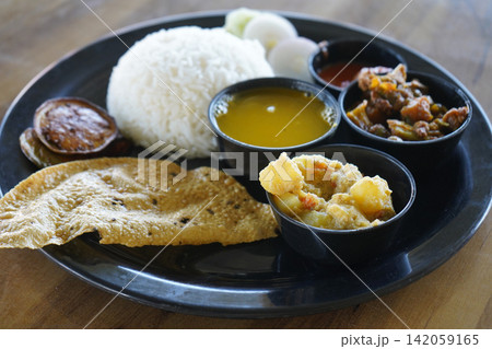 Traditional Bengali vegetarian thali meal featuring rice dal potato curry and papad on a black plate Traditional Bengali vegetarian thali meal featuring rice dal potato curry and papad on a black plate 142059165
