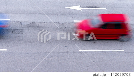 Fast moving compact car with motion blur driving on asphalt city road during rush hour. Urban transportation, travel, traffic flow, fuel consumption and modern mobility concepts. Road traffic. Fast moving compact car with motion blur driving on asphalt city road during rush hour. Urban transportation, travel, traffic flow, fuel consumption and modern mobility concepts. Road traffic. 142059708