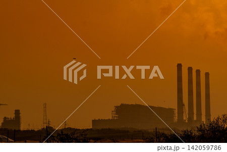 Power station chimneys rising through warm orange morning haze. Industrial energy production, electricity infrastructure, sustainability transition and climate awareness. Industrial engineering. 142059786