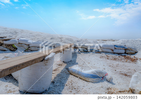 Organic sea salt storage area with wooden plank, white salt piles and plastic sacks in coastal production facility, sustainable raw material for industrial food processing. Traditional salt production 142059803