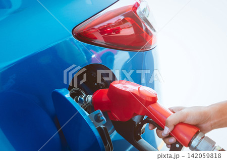 Closeup of gasoline fuel nozzle refueling a blue passenger car at a service station, transportation energy. Fuel consumption, automotive industry, travel and rising fuel costs. Gasoline consumption. Closeup of gasoline fuel nozzle refueling a blue passenger car at a service station, transportation energy. Fuel consumption, automotive industry, travel and rising fuel costs. Gasoline consumption. 142059818