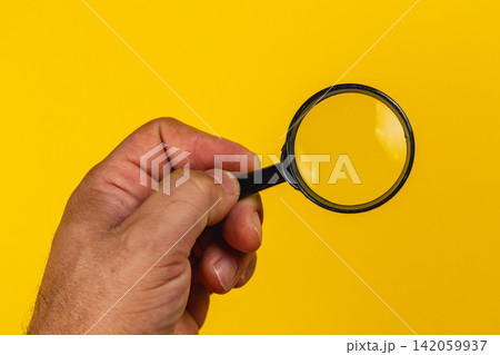 Hand holding a magnifying glass against a bright yellow background Hand holding a magnifying glass against a bright yellow background 142059937