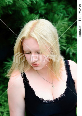 17 years old Russian blonde teenager girl looks down thoughtfully against green pine tree. 17 years old Russian blonde teenager girl looks down thoughtfully against green pine tree. 142060256