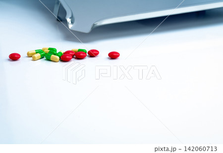 Red round sugar coated tablets and green-yellow capsules with stainless steel drug tray on white table. Pharmaceutics concept. Pharmaceutical industry. Pharmacy products. Healthcare and medication. Red round sugar coated tablets and green-yellow capsules with stainless steel drug tray on white table. Pharmaceutics concept. Pharmaceutical industry. Pharmacy products. Healthcare and medication. 142060713