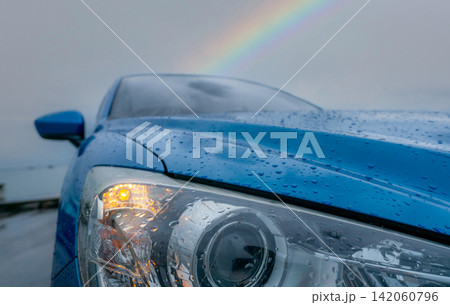 Blue passenger car covered with raindrops beneath a rainbow after rainfall, representing hope, safe transportation, weather change, recovery, resilience and new beginnings after the storm. Blue passenger car covered with raindrops beneath a rainbow after rainfall, representing hope, safe transportation, weather change, recovery, resilience and new beginnings after the storm. 142060796