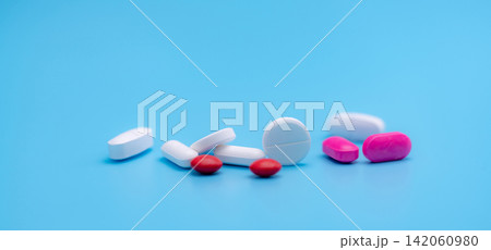 Pharmacy banner. White and pink tablets pills on blue background. Round and oval tablets. Painkiller medicine. Acetaminophen and ibuprofen tablets pills. Pharmaceutical industry. Painkiller tablets. 142060980