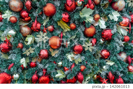 Close up of richly decorated Christmas tree with red baubles, glitter ornaments, evergreen branches and festive decorations creating vibrant holiday background for Christmas and New Year celebrations. 142061013
