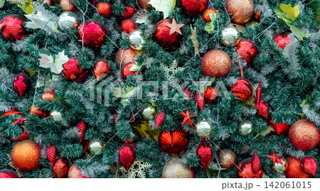 Close up of richly decorated Christmas tree with red baubles, glitter ornaments, evergreen branches and festive decorations creating vibrant holiday background for Christmas and New Year celebrations. 142061015