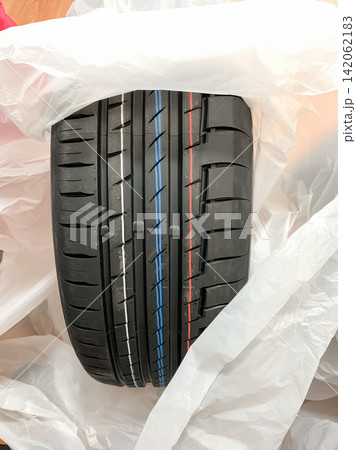 New black summer tire with colorful tread stripes unwrapped from plastic packaging New black summer tire with colorful tread stripes unwrapped from plastic packaging 142062183