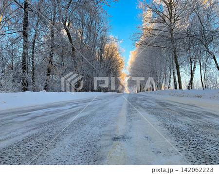 An icy road leads through a frozen forest with snow covered trees under a clear blue sky on a bright sunny winter morning An icy road leads through a frozen forest with snow covered trees under a clear blue sky on a bright sunny winter morning 142062228