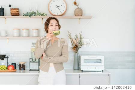 キッチンカウンターでデトックスウォーターを飲む女性 キッチンカウンターでデトックスウォーターを飲む女性 142062410