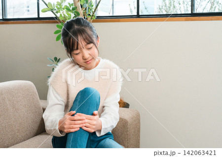 自宅のソファに座り膝痛で膝,脛を抑える小学生,中学生の女の子 自宅のソファに座り膝痛で膝,脛を抑える小学生,中学生の女の子 142063421