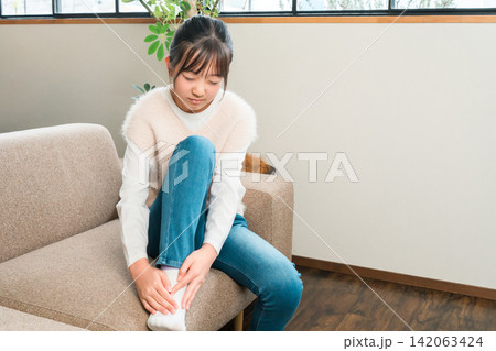 自宅のソファに座り足首を抑える小学生,中学生の女の子 自宅のソファに座り足首を抑える小学生,中学生の女の子 142063424