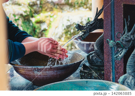 神社の手水舎で龍の水口から流れる水で手を清める参拝者 神社の手水舎で龍の水口から流れる水で手を清める参拝者 142063885