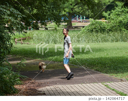 真夏の公園で可愛いポメラニアンの子犬を連れて散歩する夏休み中の女子学生の姿 真夏の公園で可愛いポメラニアンの子犬を連れて散歩する夏休み中の女子学生の姿 142064717