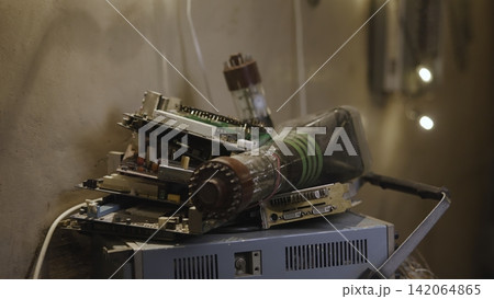 Stacked vintage circuit boards with glass vacuum tubes on metal chassis inside warm workshop storage, showing worn electronics, cables, solder points, and industrial textures Stacked vintage circuit boards with glass vacuum tubes on metal chassis inside warm workshop storage, showing worn electronics, cables, solder points, and industrial textures 142064865
