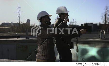 Two Professionals Walking Rooftop Together Discussing Timeline Tasks And Referencing Tablet For Coordination. Media 142064989