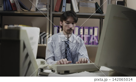 Office worker typing at desk in archive room Office worker typing at desk in archive room 142065014