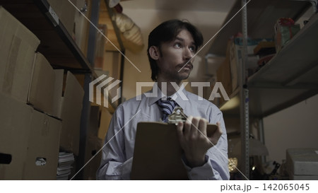 Office worker reviewing inventory among storage shelves 142065045