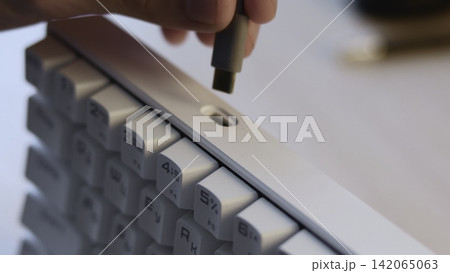 Close-up cable plug connecting into recessed port on white keyboard, showing precise insertion, shallow depth focus, clean workspace details and modern computer interaction Close-up cable plug connecting into recessed port on white keyboard, showing precise insertion, shallow depth focus, clean workspace details and modern computer interaction 142065063