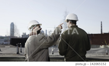 Construction workers discussing plans on an industrial rooftop with city skyline 142065152
