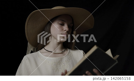 Woman in a Straw Hat Reading a Book in Soft Dark Studio Light Woman in a Straw Hat Reading a Book in Soft Dark Studio Light 142065158