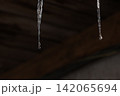 Melting icicles and falling water drops: Close-up of spring thaw on blurred wooden background 142065694