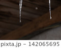 Melting icicles and falling water drops: Close-up of spring thaw on blurred wooden background 142065695