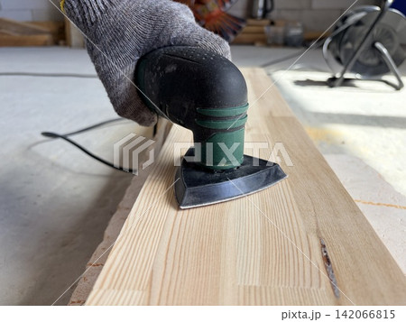 a worker's hand wearing a grey knitted protective glove operating an electric detail sander. Renovation or construction work a worker's hand wearing a grey knitted protective glove operating an electric detail sander. Renovation or construction work 142066815