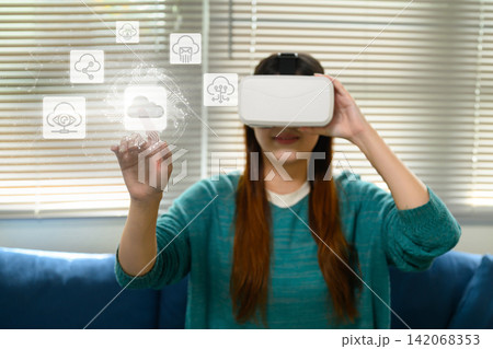 Asian Woman Wearing VR Headset Touching Virtual Cloud Computing Icons in Futuristic Digital Interface Asian Woman Wearing VR Headset Touching Virtual Cloud Computing Icons in Futuristic Digital Interface 142068353