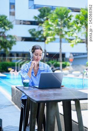 Professional businesswoman working on laptop by the hotel pool during vacation, representing remote work, digital nomad lifestyle Professional businesswoman working on laptop by the hotel pool during vacation, representing remote work, digital nomad lifestyle 142068362
