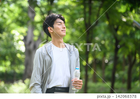 Young Asian Man Resting Outdoors After Exercise Holding Water Bottle in Green Park 142068378