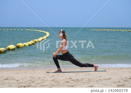 Woman performing yoga lunge on beach with copy space and ocean view 142068379