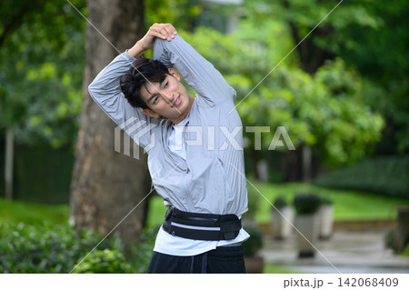 Young Asian Man Stretching Arms Outdoors in Park Before Running Workout in Sportswear 142068409