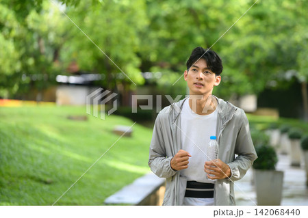 Young Asian Man Walking in Park Holding Water Bottle After Workout 142068440