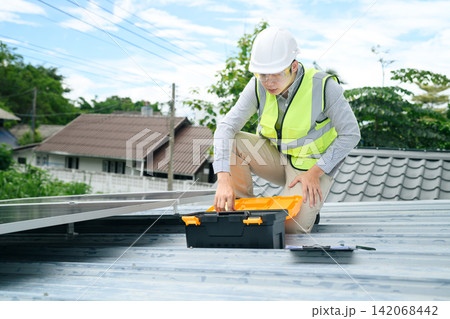Solar Panel Technician Installing Photovoltaic System on Residential Rooftop with Toolbox 142068442