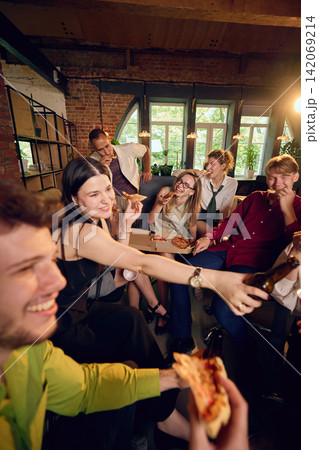 Coworker passing pizza slice across crowded office party table Coworker passing pizza slice across crowded office party table 142069214