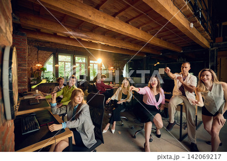 Coworker plays darts while confused office colleagues watch during company party. Coworker plays darts while confused office colleagues watch during company party. 142069217