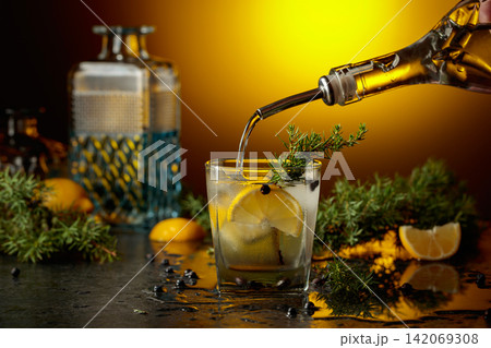 Gin is poured from a bottle into a glass with ice and lemon slice. Gin is poured from a bottle into a glass with ice and lemon slice. 142069308
