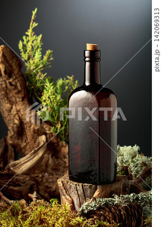 Vintage bottle of gin or herbal bitter, set among juniper branches, weathered driftwood and forest moss. Vintage bottle of gin or herbal bitter, set among juniper branches, weathered driftwood and forest moss. 142069313