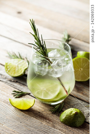 Gin tonic with ice, rosemary, and lime slices on an old wooden table. Gin tonic with ice, rosemary, and lime slices on an old wooden table. 142069333